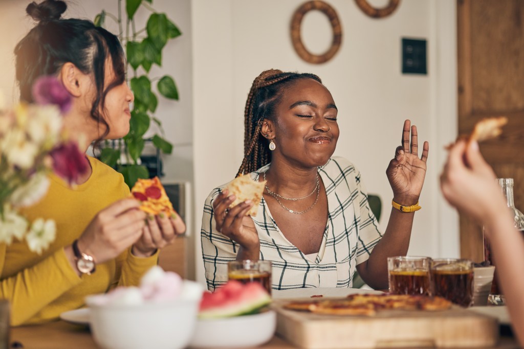 Two young women enjoying pizza and drinks at a dinner party.