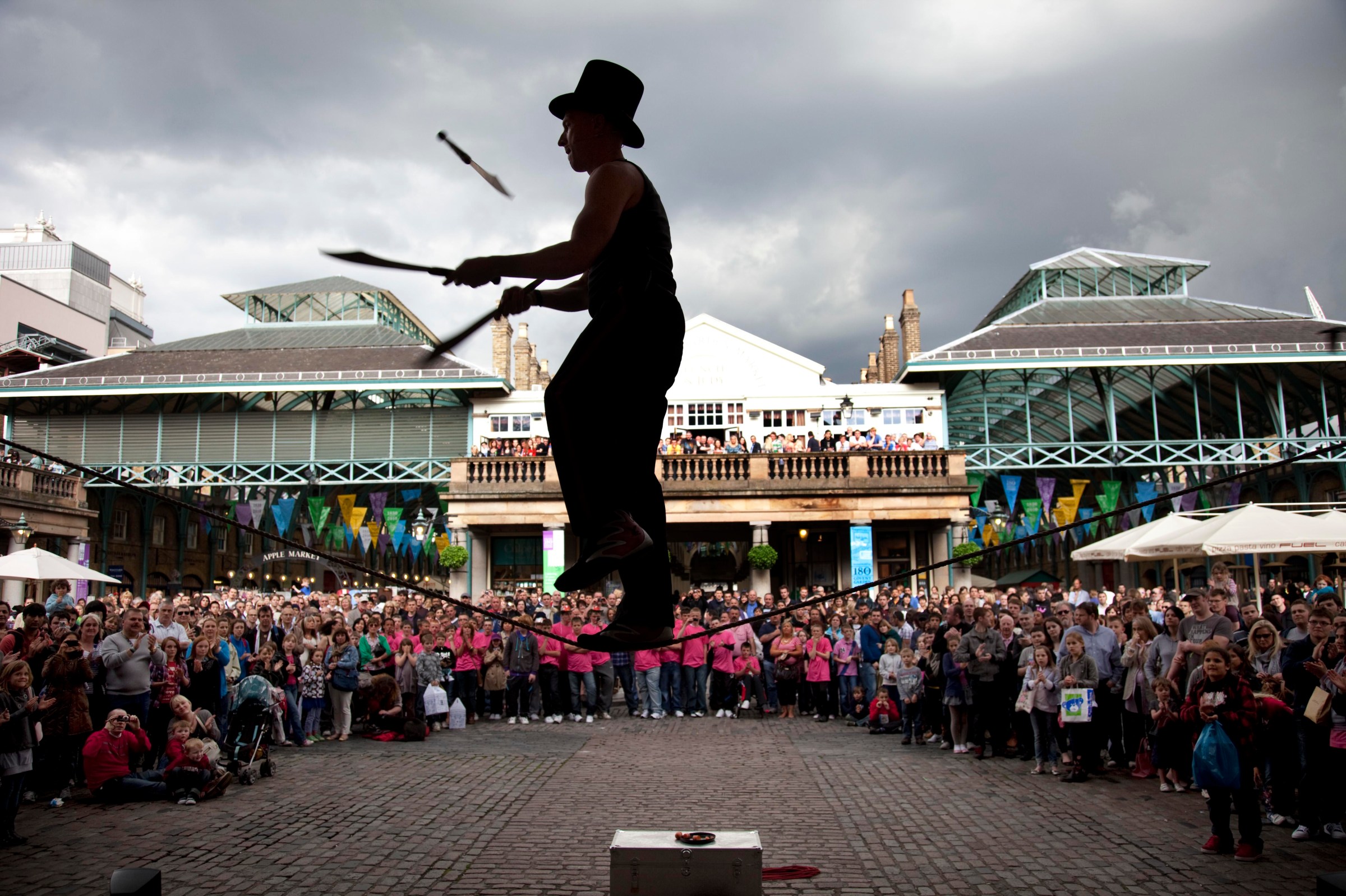 Street performer thrills the crowd with his knife juggling act whilst in a slack line. Covent Garden plaza in the West End of London. (Photo by Mike Kemp/In Pictures Ltd./Corbis via Getty Images)