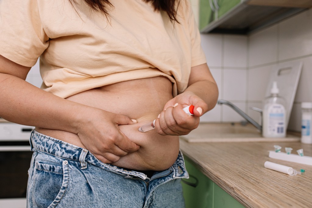 A woman gives herself a GLP-1 injection into her abdomen with a pen syringe for weight loss.