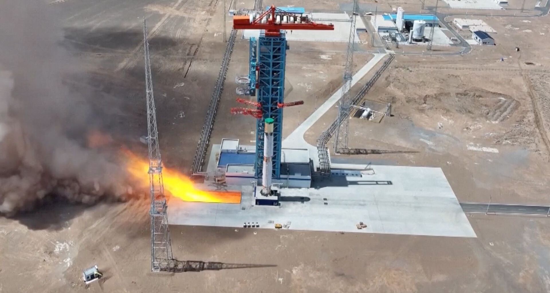 long-distance photo of a white rocket firing its engines on a launch pad