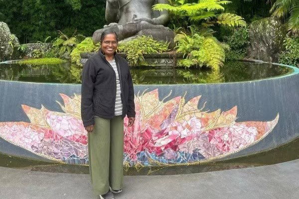 A older woman standing at a man-made pond smiling.
