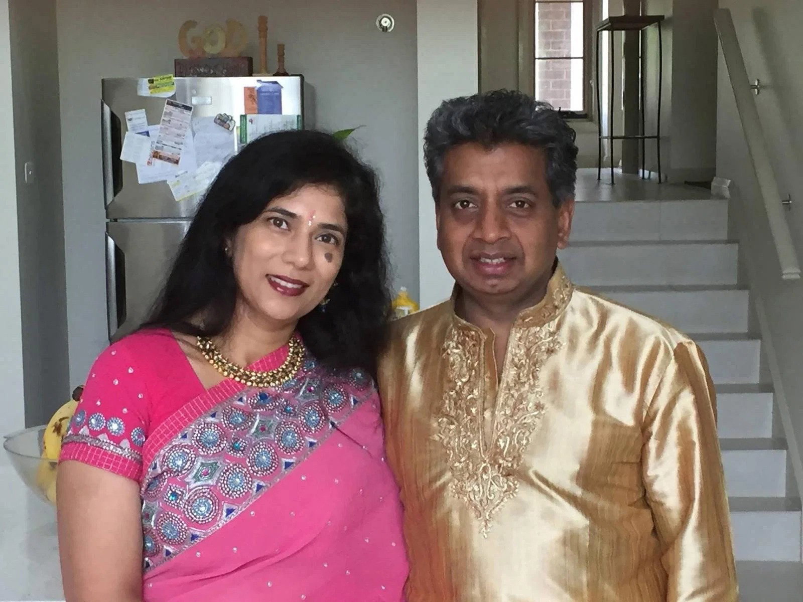 A woman and man in formal traditional attire (Sari and Kurta) posed together in their home. 