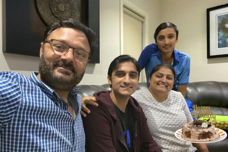 A selfie taken by a man with two younger boys in the shot and his wife holding a birthday cake. 