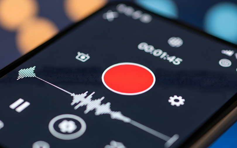 Close-up shot of a smartphone screen displaying a music player interface with a prominent red play button, audio waveform visualization, and playback controls.