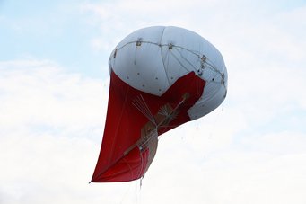 A helikite balloon in red and white with a kind of sail at the bottom of the balloon.