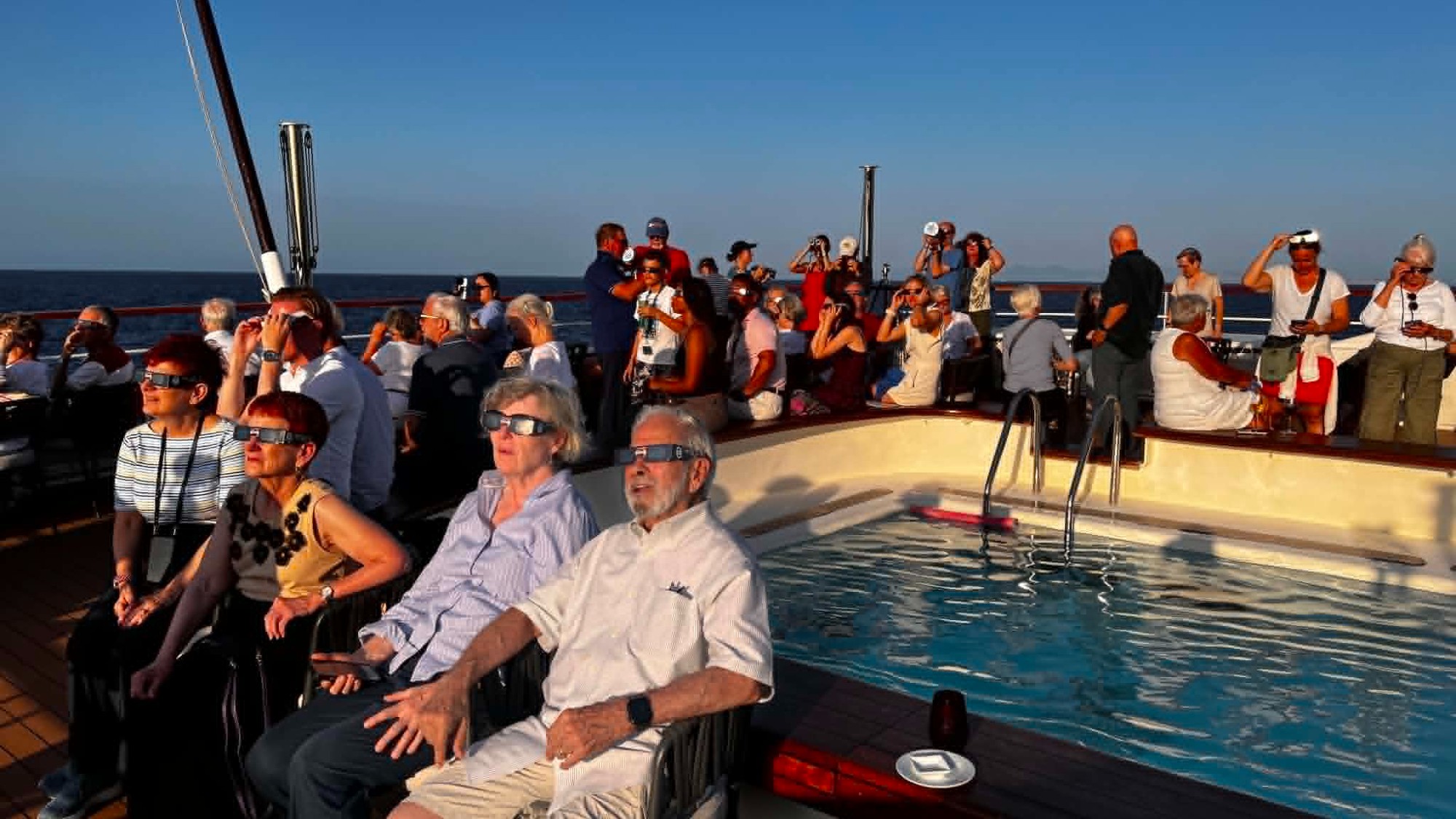 people sit on the deck of a ship wearing paper sunglasses, looking skyward