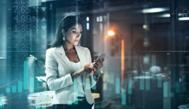 Shot of a young businesswoman using her phone at work, with stock market related images in the background.