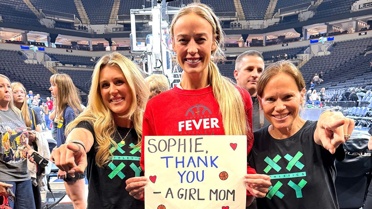 Riley Gaines, Indiana Fever guard Sophie Cunningham, and XX-XY Athletics founder Jen Sey posing together courtside with a 