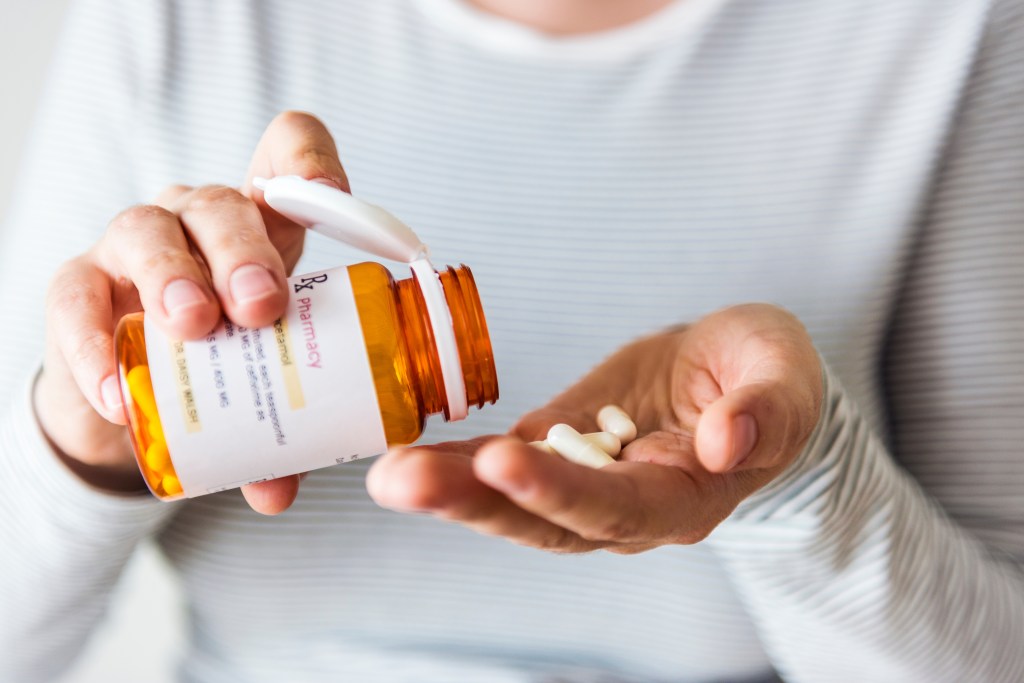 A woman pouring pills from a medicine bottle into her hand.
