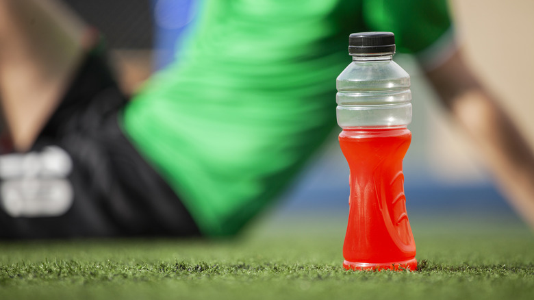 red sports drink sitting on the grass with person behind