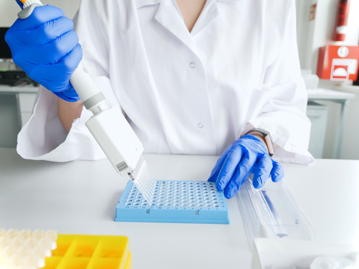 A gloved scientist in a lab uses a device to insert multiple samples into a tray with many openings.