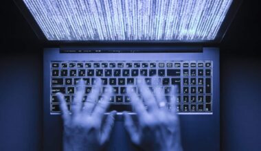 Hands typing on a laptop in the dark. Program code is visible on the screen.