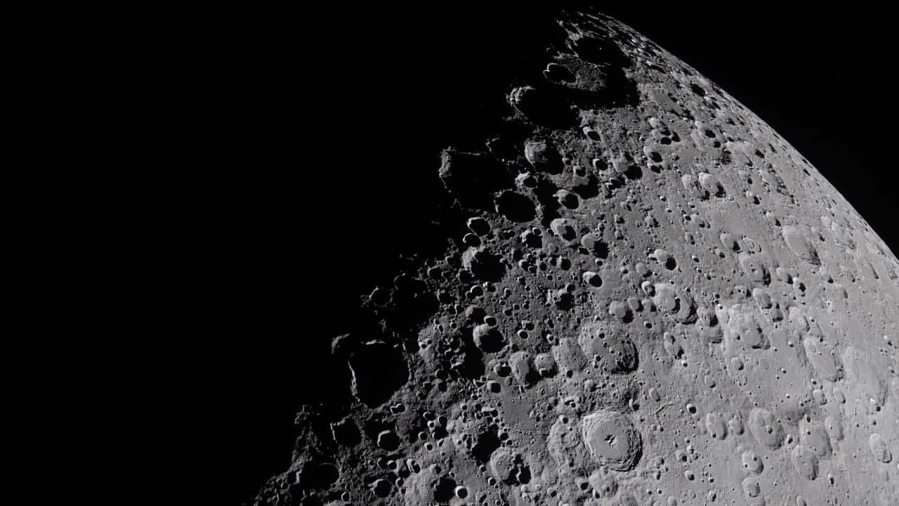 A photopgraph of the moon, taken at close range. Shadow obscures part of its face, highlighting crater edges.