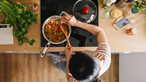 Woman adding spices to vegetables in a frying pan