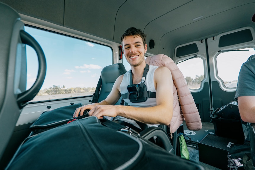 a man wearing a camera on his chest smiles sitting in a van