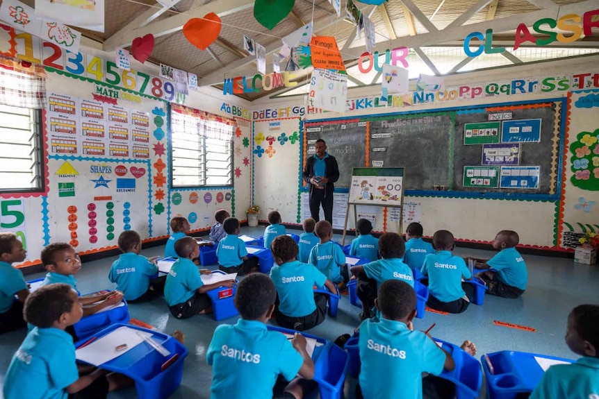 A colourful classroom of PNG children in Santos-branded turquoise T-shirts.