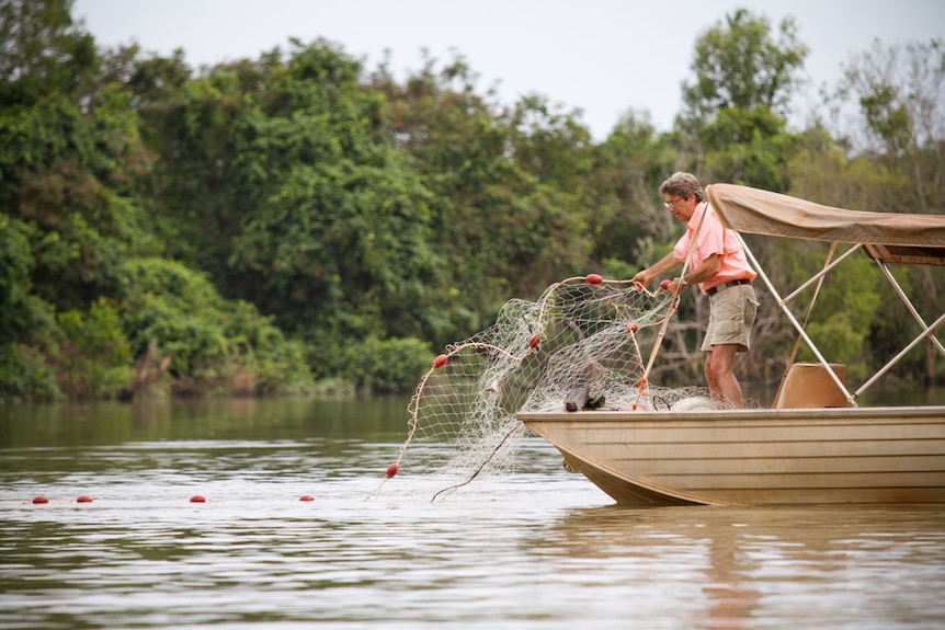 A man throwing a gillnet into a river, setting it in the water by throwing it over the side of a small boat.