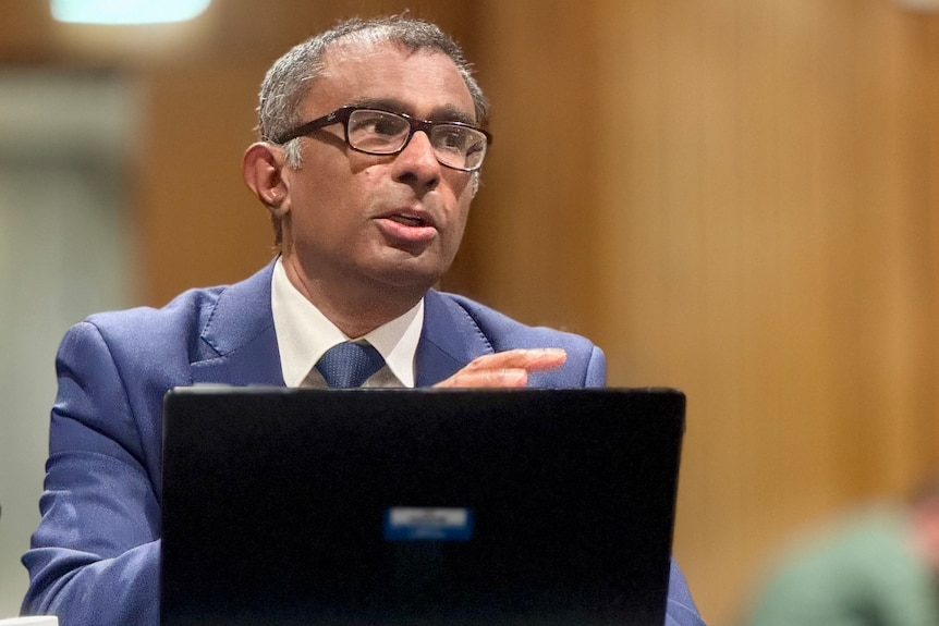A man wearing glasses speaks into a microphone.
