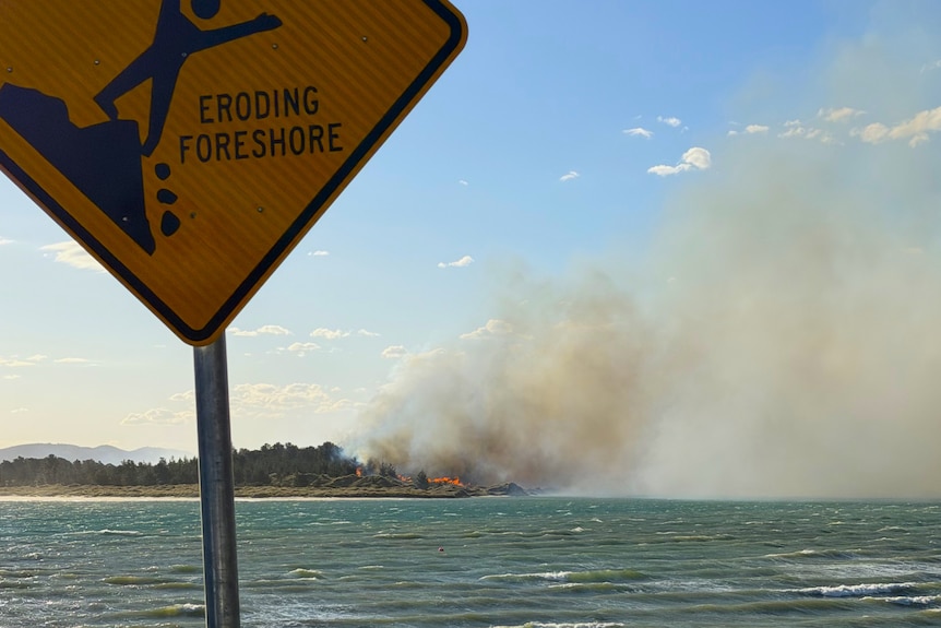 Smoke from bushfire across water with sign in foreground.