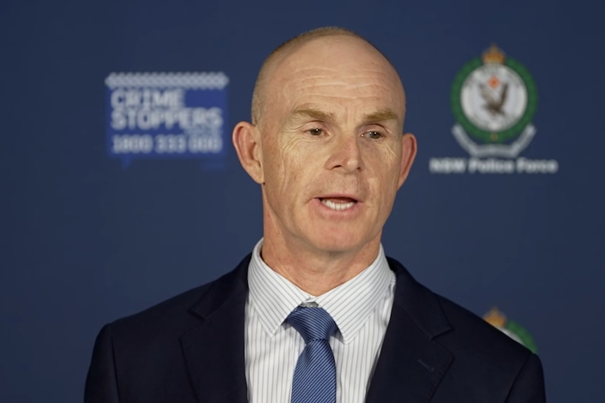 Brad Abdy speaking in a black suit, blue tie, at a police press conference.
