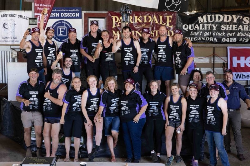 Group photo of more than 20 shearers wearing black and purple kit.