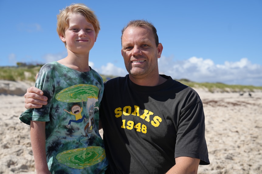 A man with black put his arm around a 8yo boy's shoulders.