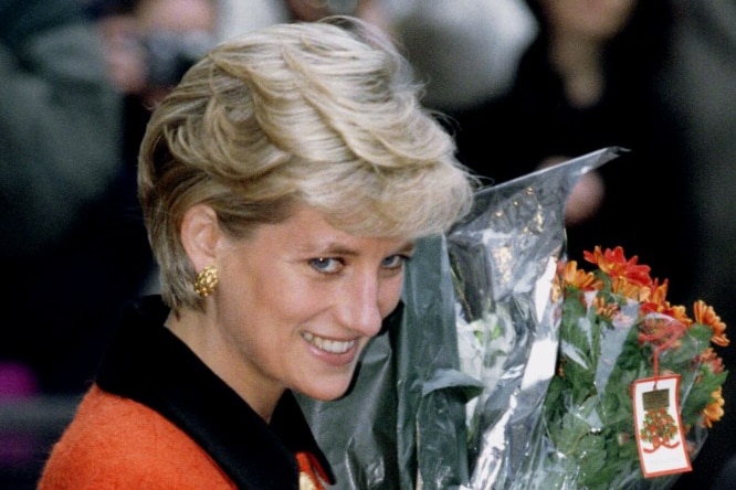 A woman carries flowers and looks on smiling.