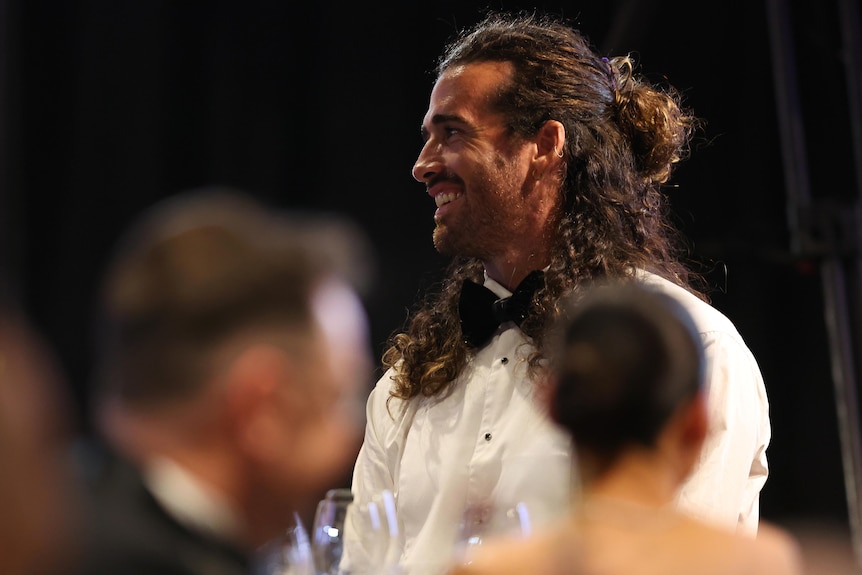 Alex Pearce wears his hair down and looks sideways, smiling.