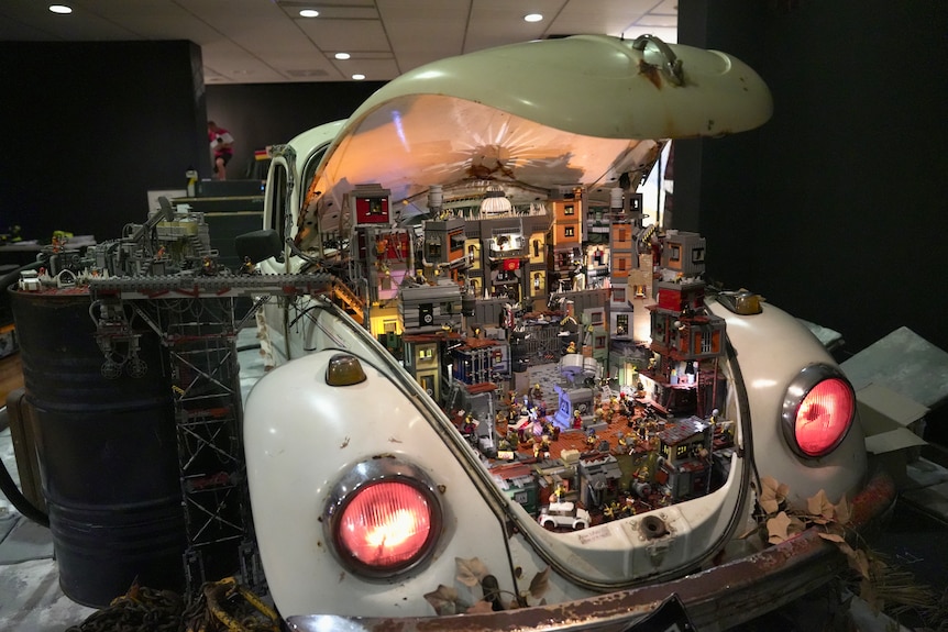 An old white Volkswagen Beetle's boot is open, revealing a bustling urban residential scene made of lego.