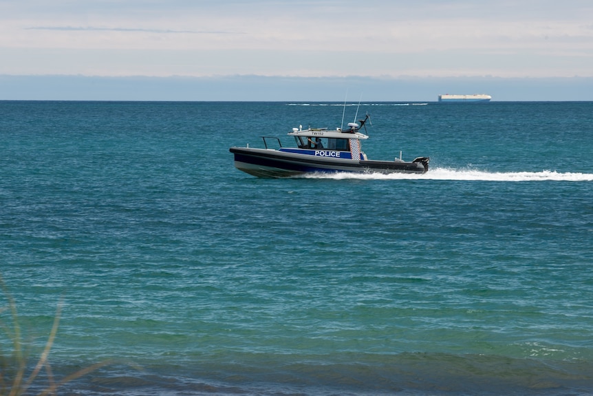 A water police speedboat travels in open ocean near the shore.