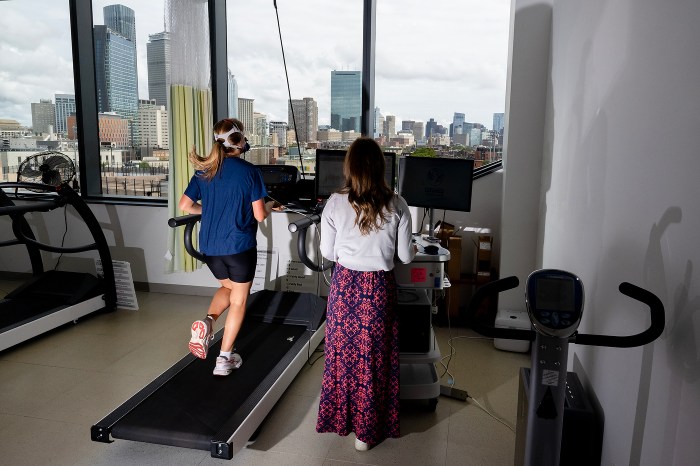 Smith runs on a treadmill facing a floor-to-ceiling window overlooking the Boston skyline while Carey monitors data at a nearby workstation.