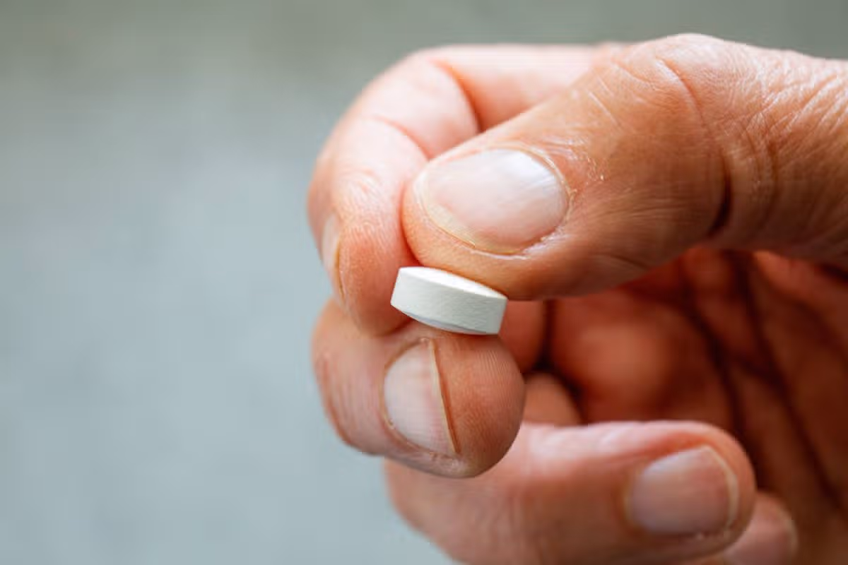 An individual is holding a small, cylindrical white object, presumably a pill or tablet, between their fingers, with a focus on the precision and detail of the object.