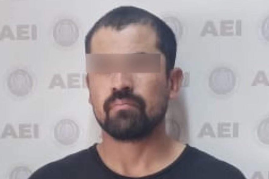 A mugshot of a bearded man wearing a black t-shirt, with a blurred bar over his eyes.