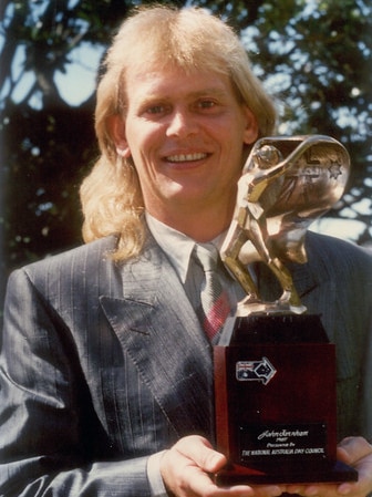 A young John Farnham with long hair, holding an award after being named Australian of the Year.