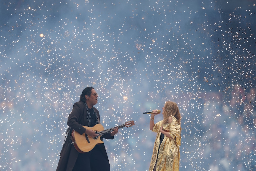 William Barton wearing a long black coat and Kylie Minogue in a metallic gold coat