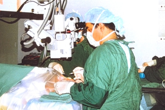 A man in hospital scrubs operates on a person's eye.