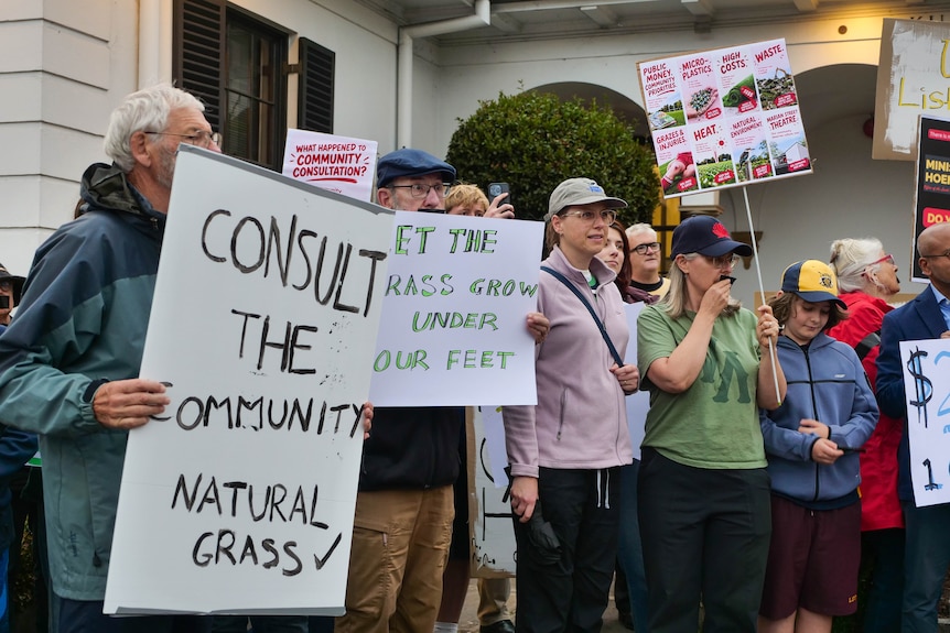 a small crowd holding signs protesting a football field