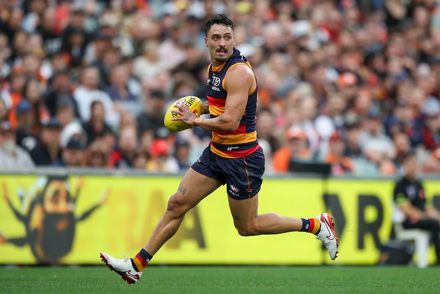 Izak Rankine running with the ball, looking for a teammate to kick to in an AFL match