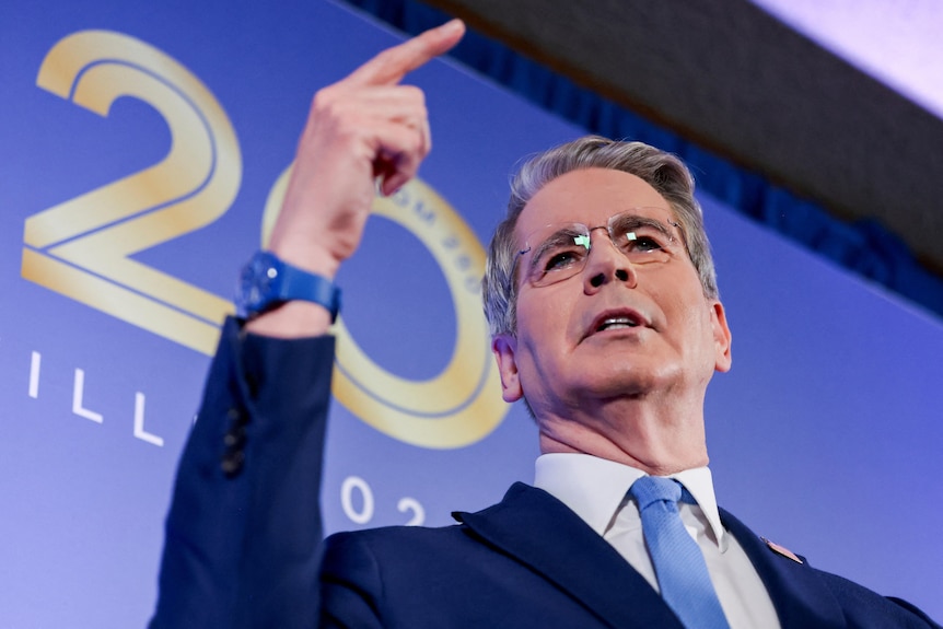 U.S. Treasury Secretary Scott Bessent gestures in front of a banner with the graphic of 20 in front of it.