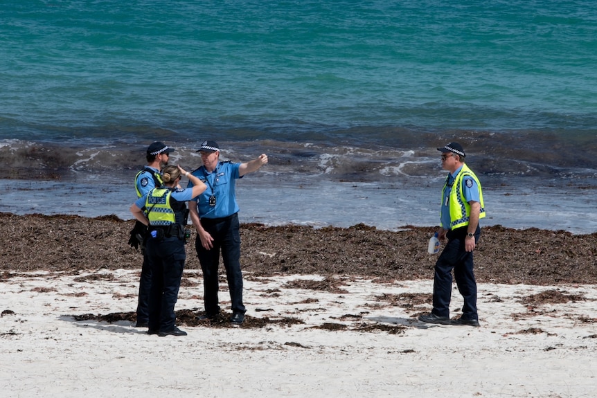 Four police officers stand on beach near shoreline 