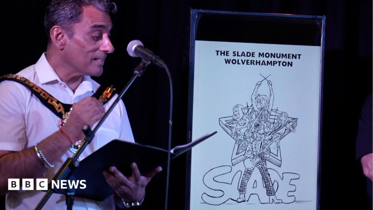 A man is wearing a white shirt and is standing in front of a microphone, next to a drawing of a monument.