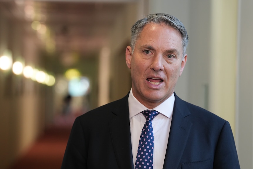A man in a suit and tie speaking in a corridor.