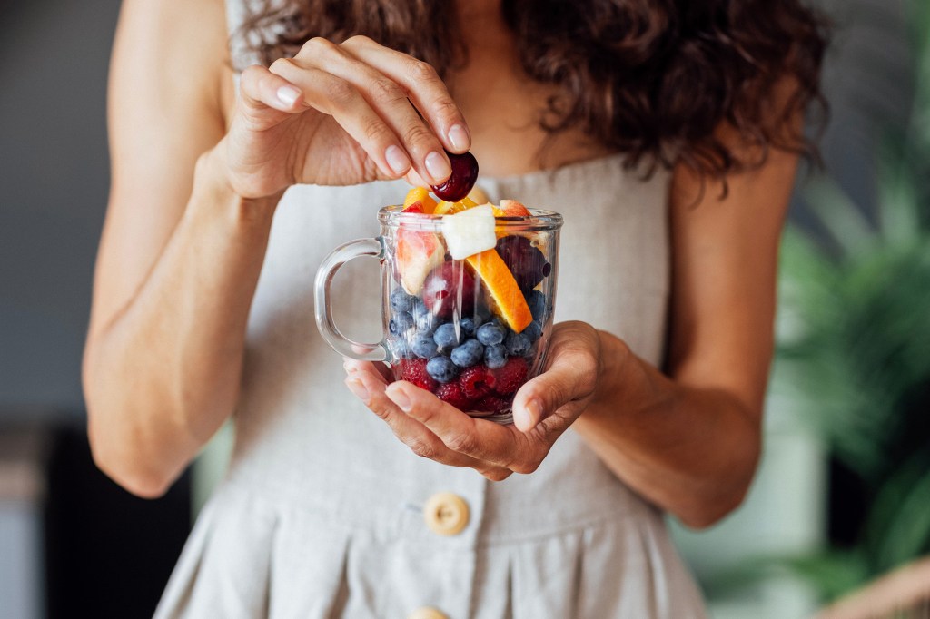 A person adding a cherry to a glass mug full of fruit.