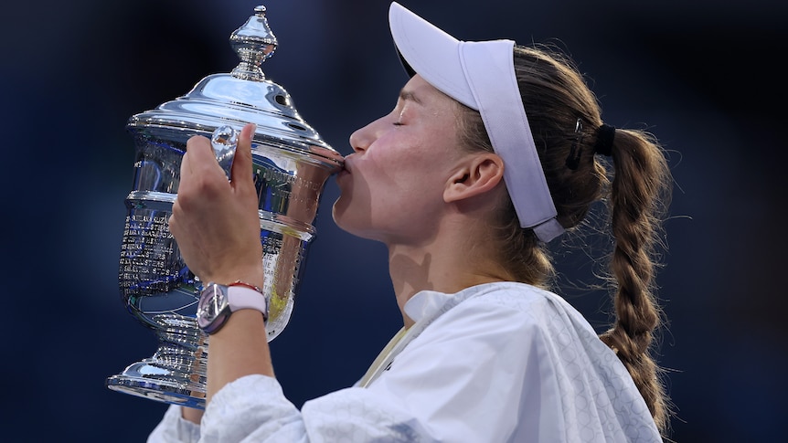 A side-on shot of a women's tennis player kissing a trophy.