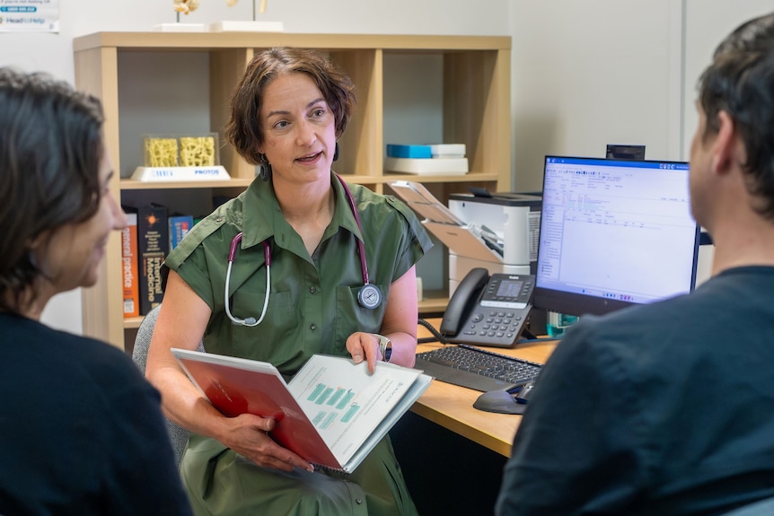 a female doctor in green scrubs talks to two people