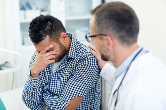 A doctor comforts a distressed male patient, discussing standard medical procedures.