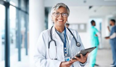Doctor with stethoscope holding a tablet and smiling.