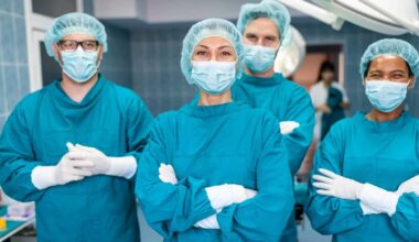 a group of surgeons in full surgery dress including masks, gloves and head coverings stands together with arms folded and smiling eyes as if happy with the outcome of their efforts.