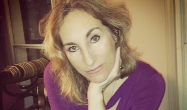 A woman with long, wavy light-coloured hair with her hand propping up her chin.