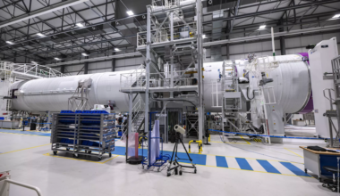 aerospace manufacturing hangar with a white cylindrical spacecraft
